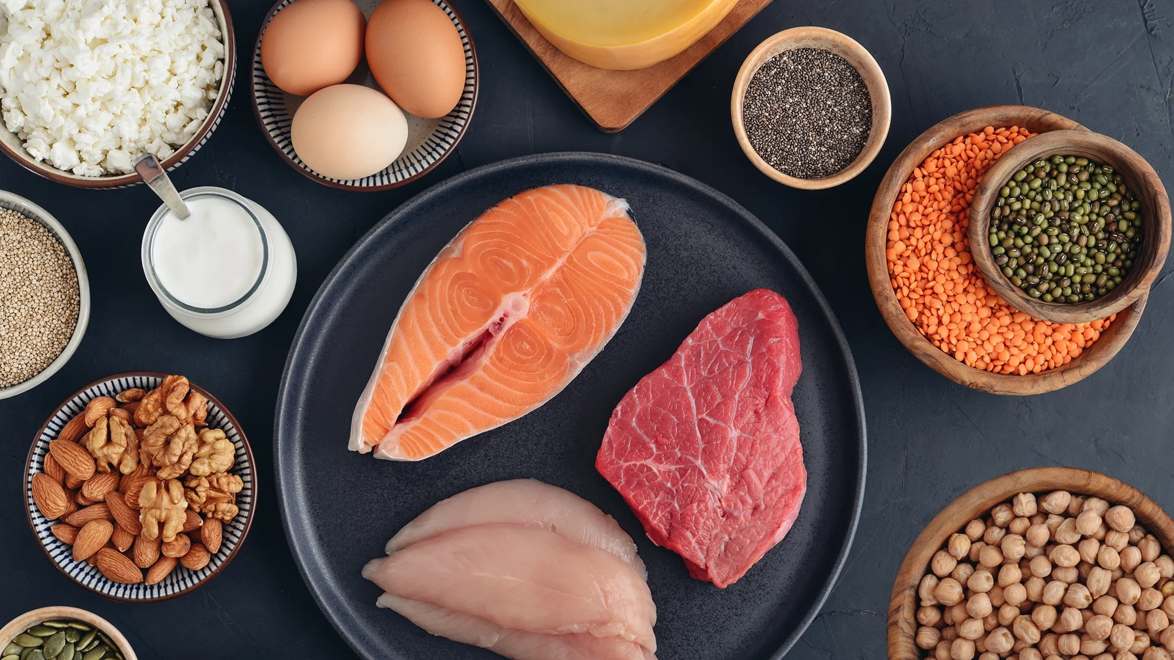 Raw meat, cheese, nuts, eggs, and beans lie on a black surface.