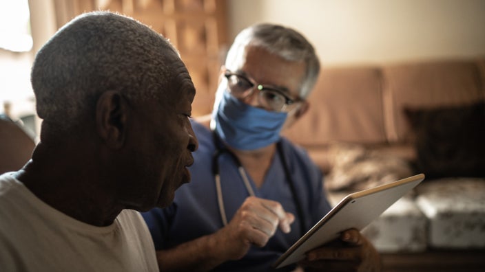 Nurse talking with patient at home going over information on a tablet.