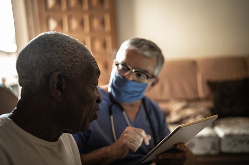 Nurse talking with patient at home going over information on a tablet.