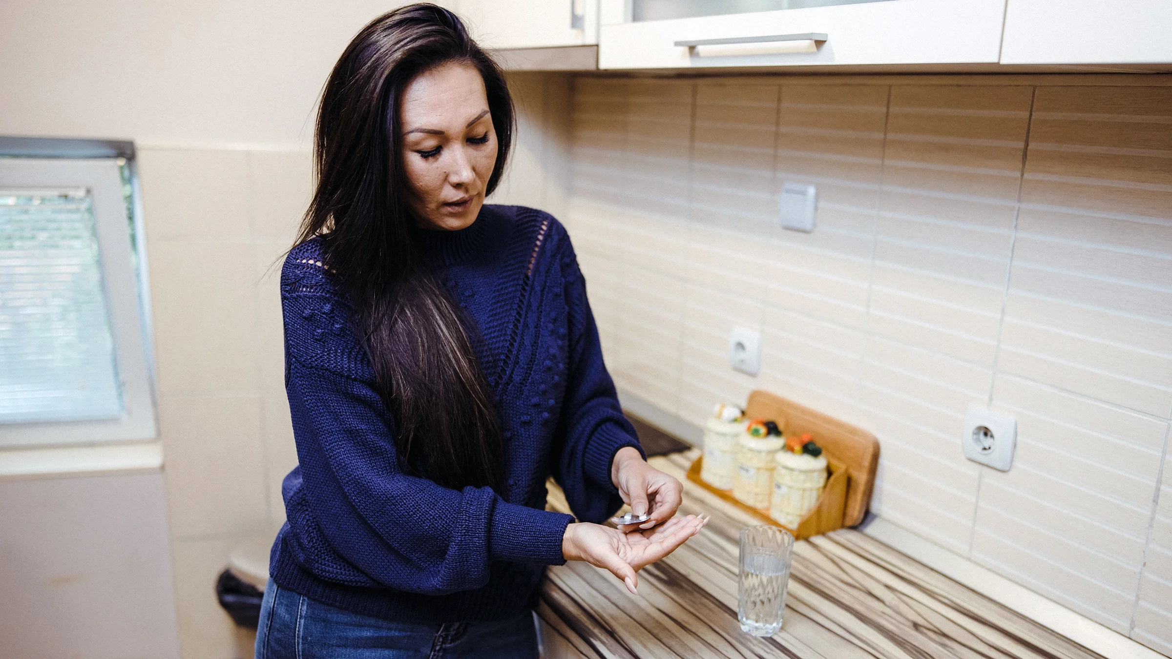 A woman takes a pill from a blister pack in her kitchen.