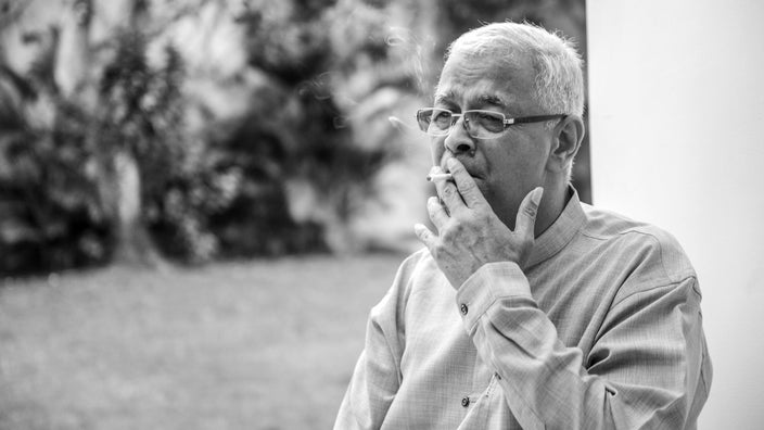 Black and white portrait of a senior man smoking a cigarette outside.