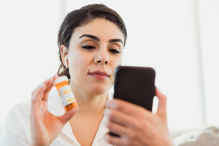 Woman on a telehealth visit on her phone showing a prescription bottle to the camera with a neutral look on her face.