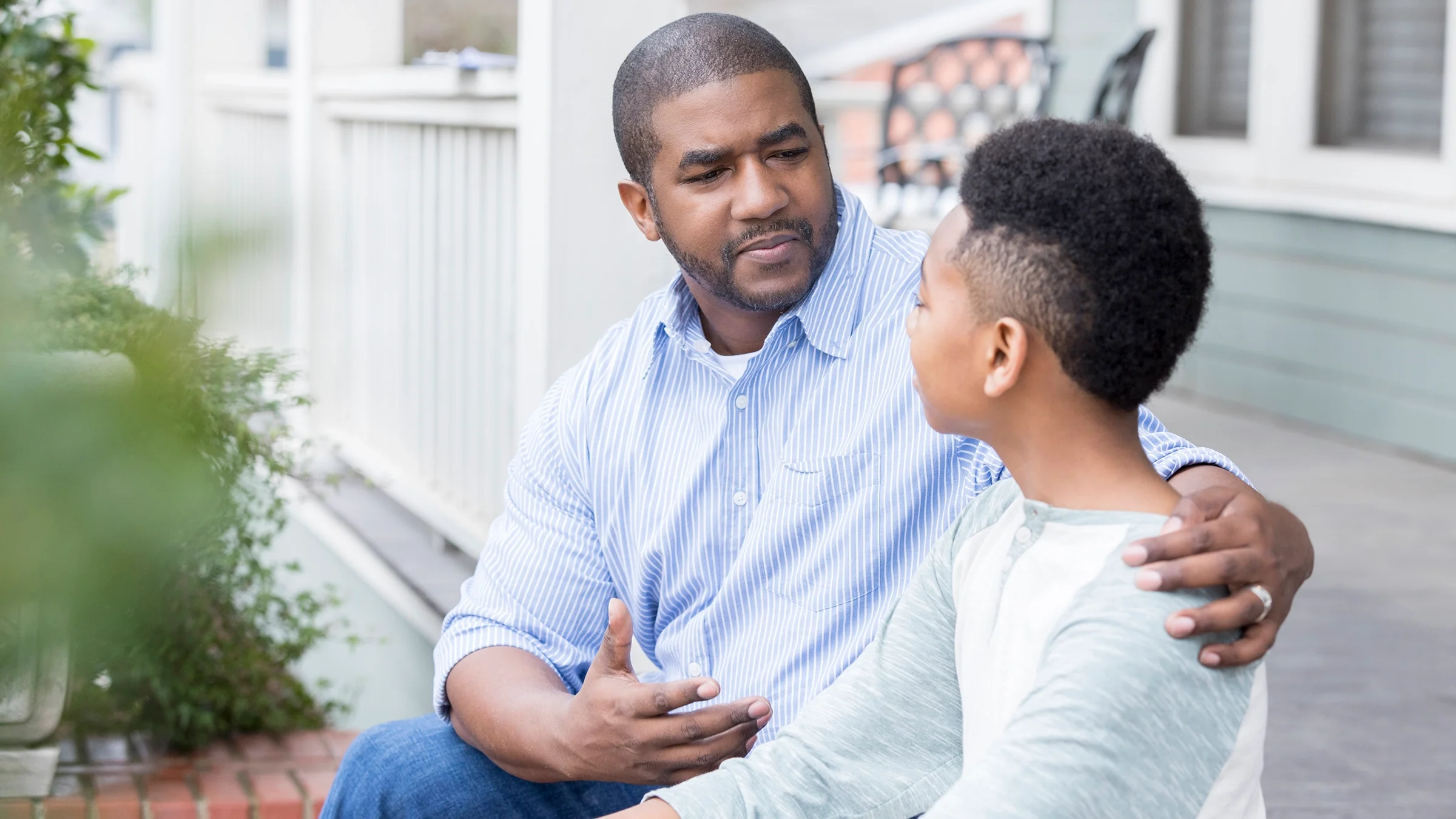Father talking to son on front porch of house.