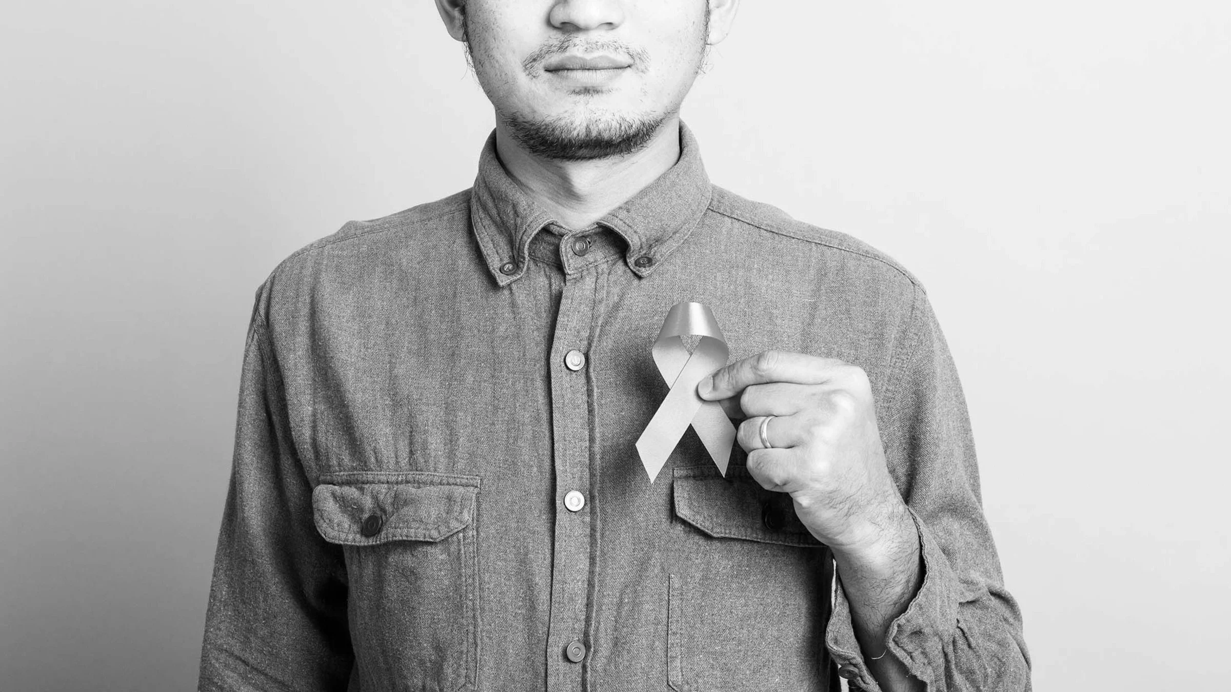 Black and white cropped shot of a man holding a cause ribbon in front of his chest.