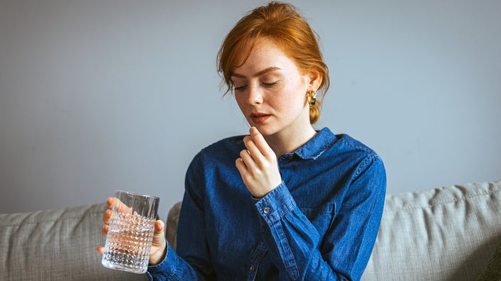 A woman prepares to take a pill with a glass of water.