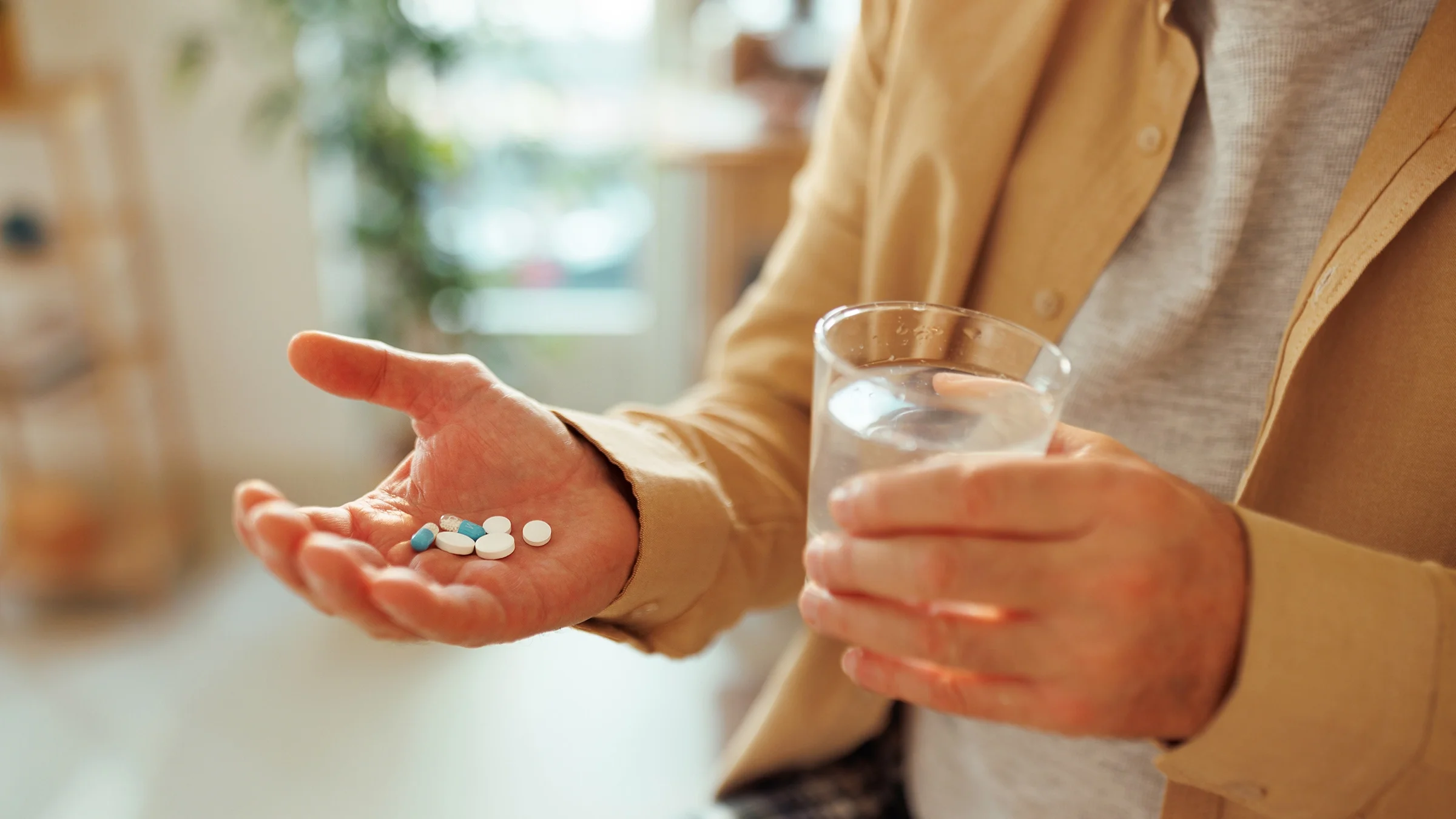 Close-up of a hand with pills and a glass of water.