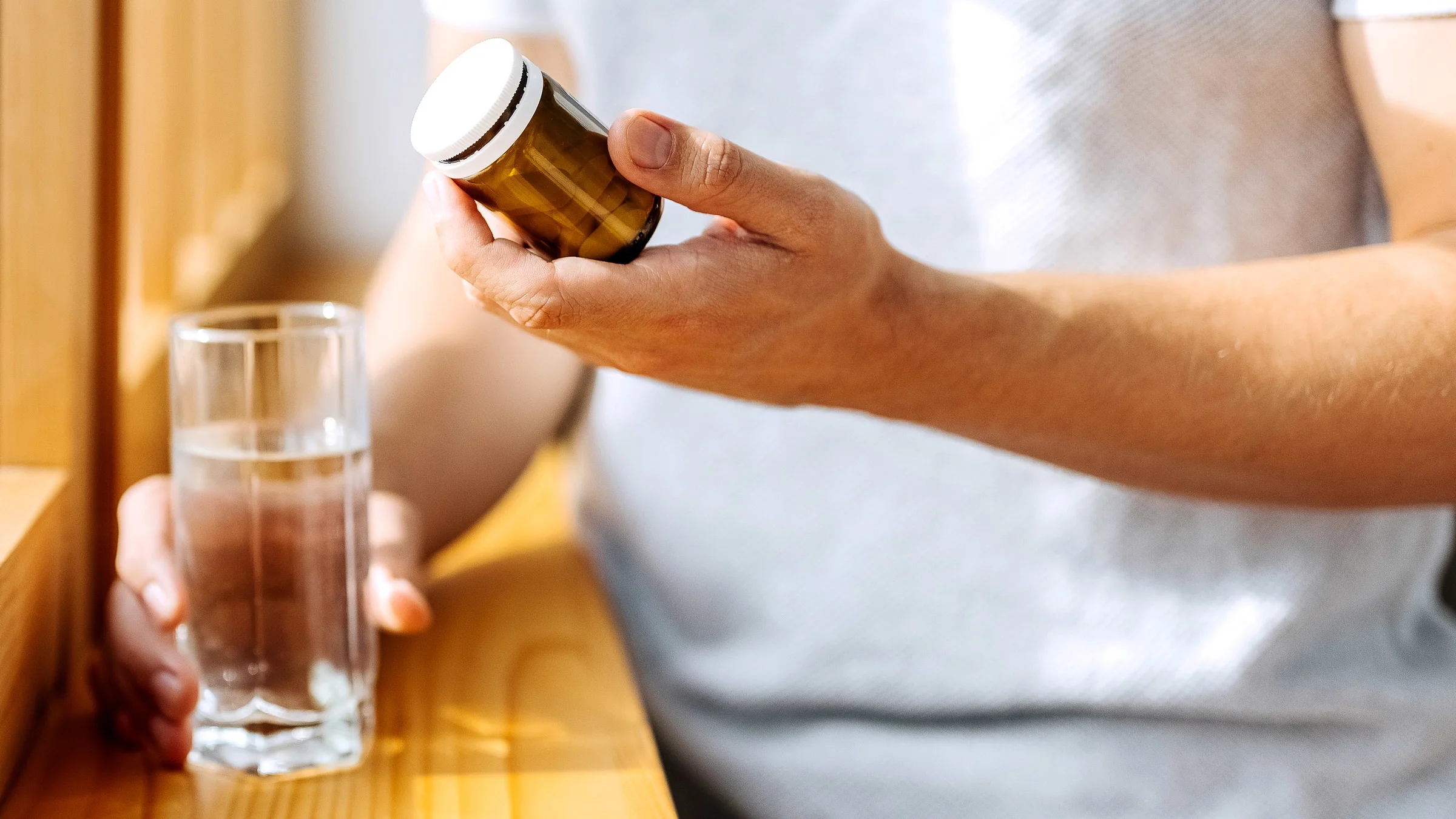 Close-up of a man holding a supplement bottle and a cup of water.