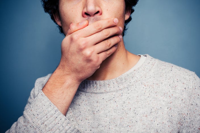 Cropped portrait of a man covering his mouth on a blue gradient background.
