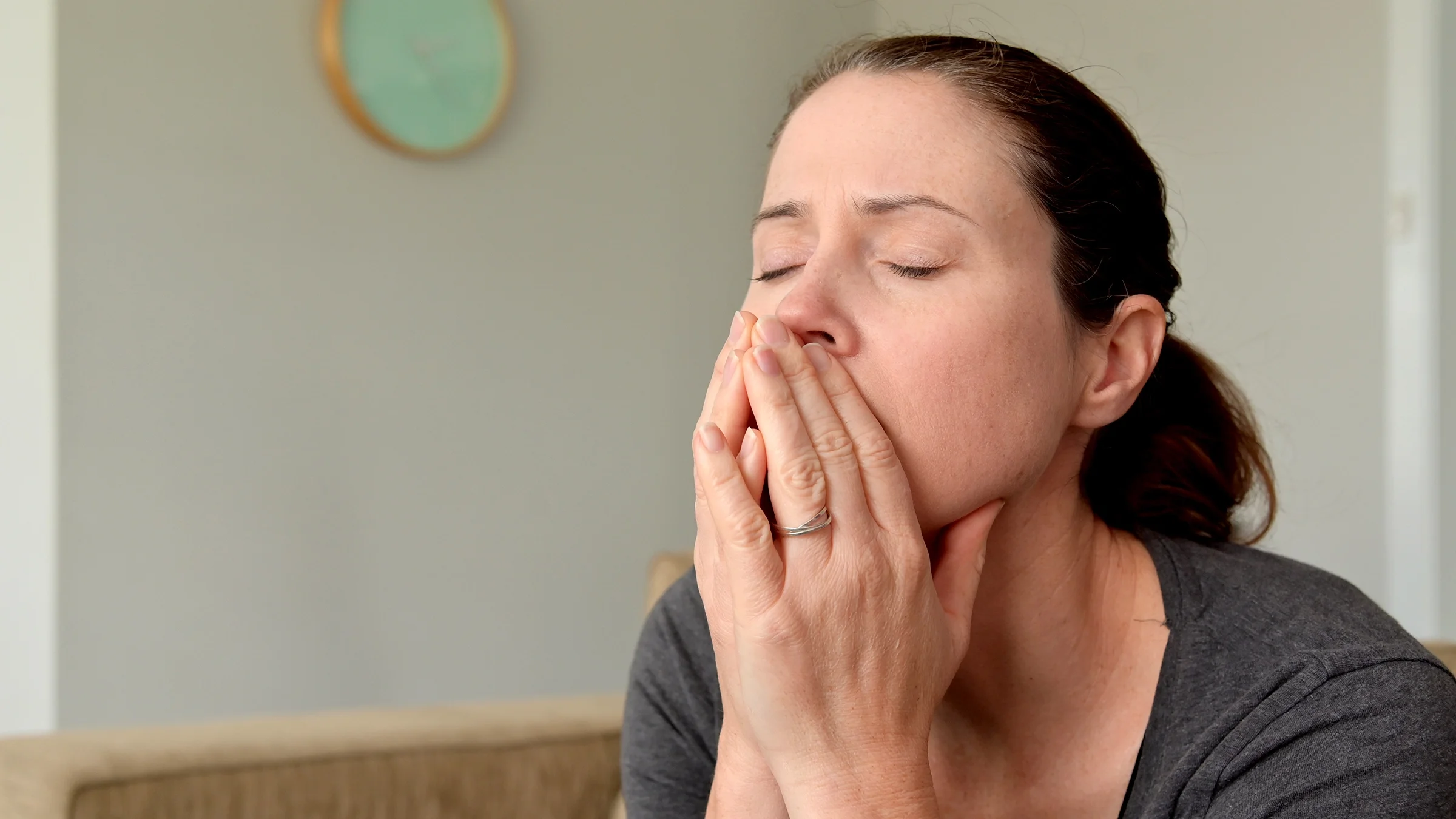 A woman closes her eyes as she brings her hands to her nose. 