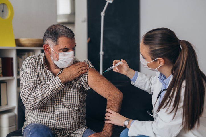 Older man rolling up his sleeve getting a vaccine administered by a doctor.