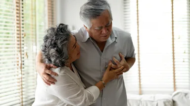 An older man having a heart attack, being supported by his wife.
eggeeggjiew/iStock via Getty Images Plus  