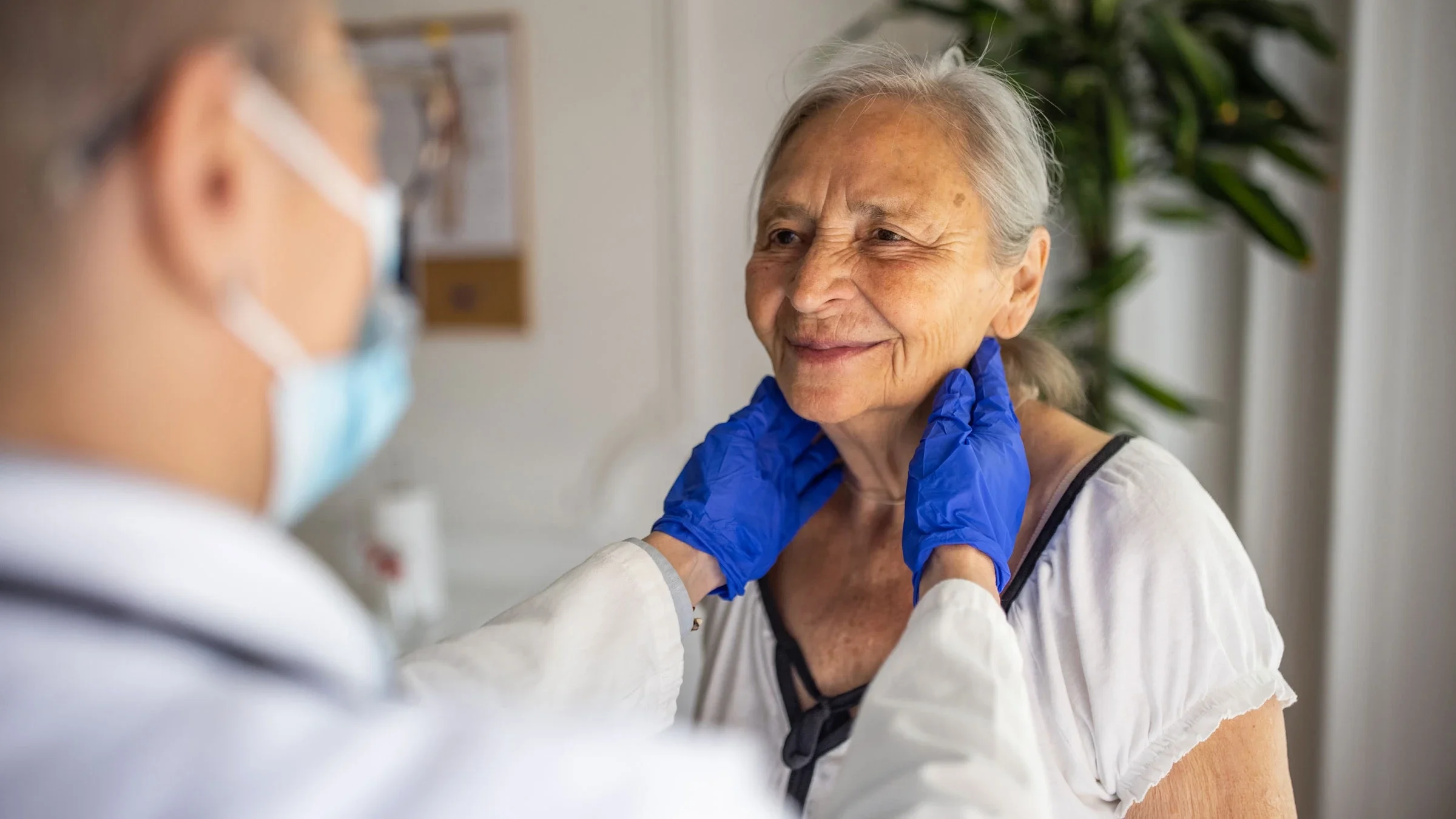 A healthcare provider is examining an older adult while palpating their lymph nodes.