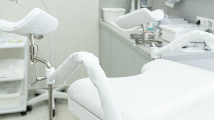 A white gynecological exam chair sits empty in a medical clinic.