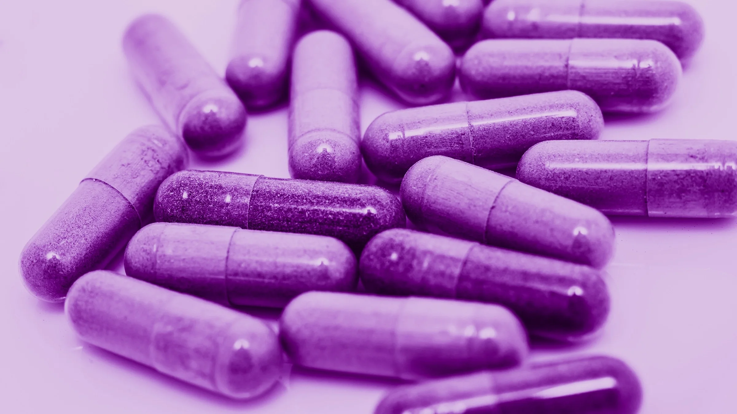 Close-up of a pile of purple capsule pills on a light purple background.