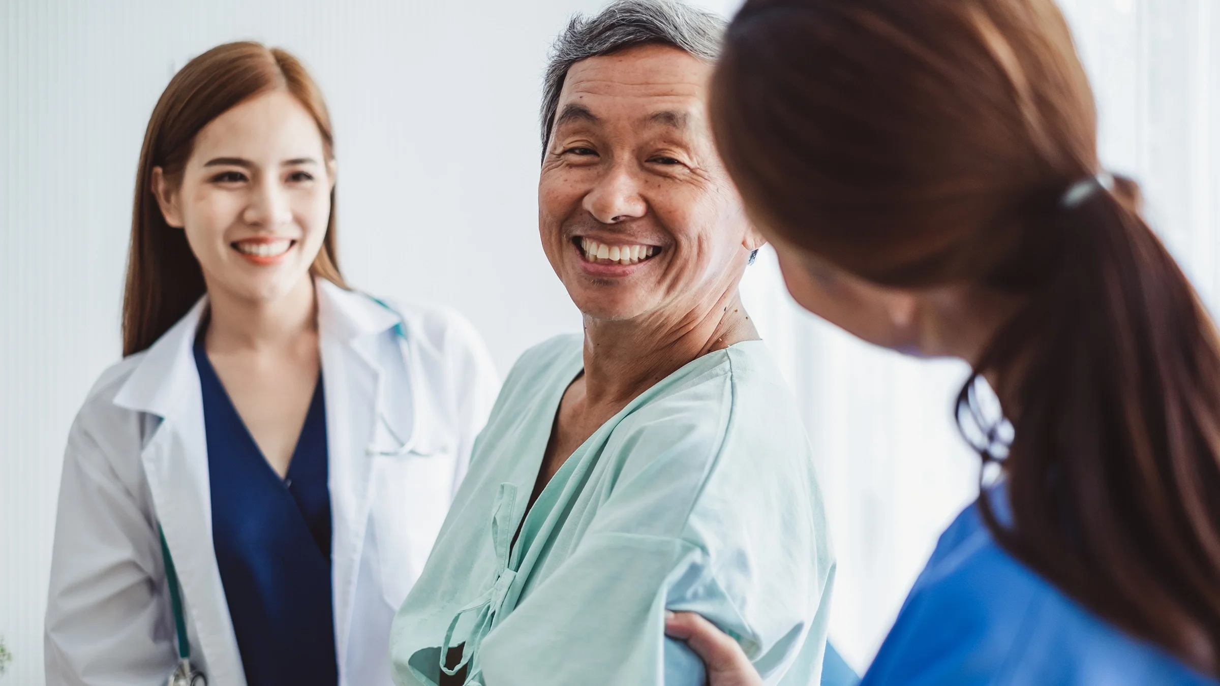 Senior man in hospital gown smiling at his doctor and nurse who are helping him.