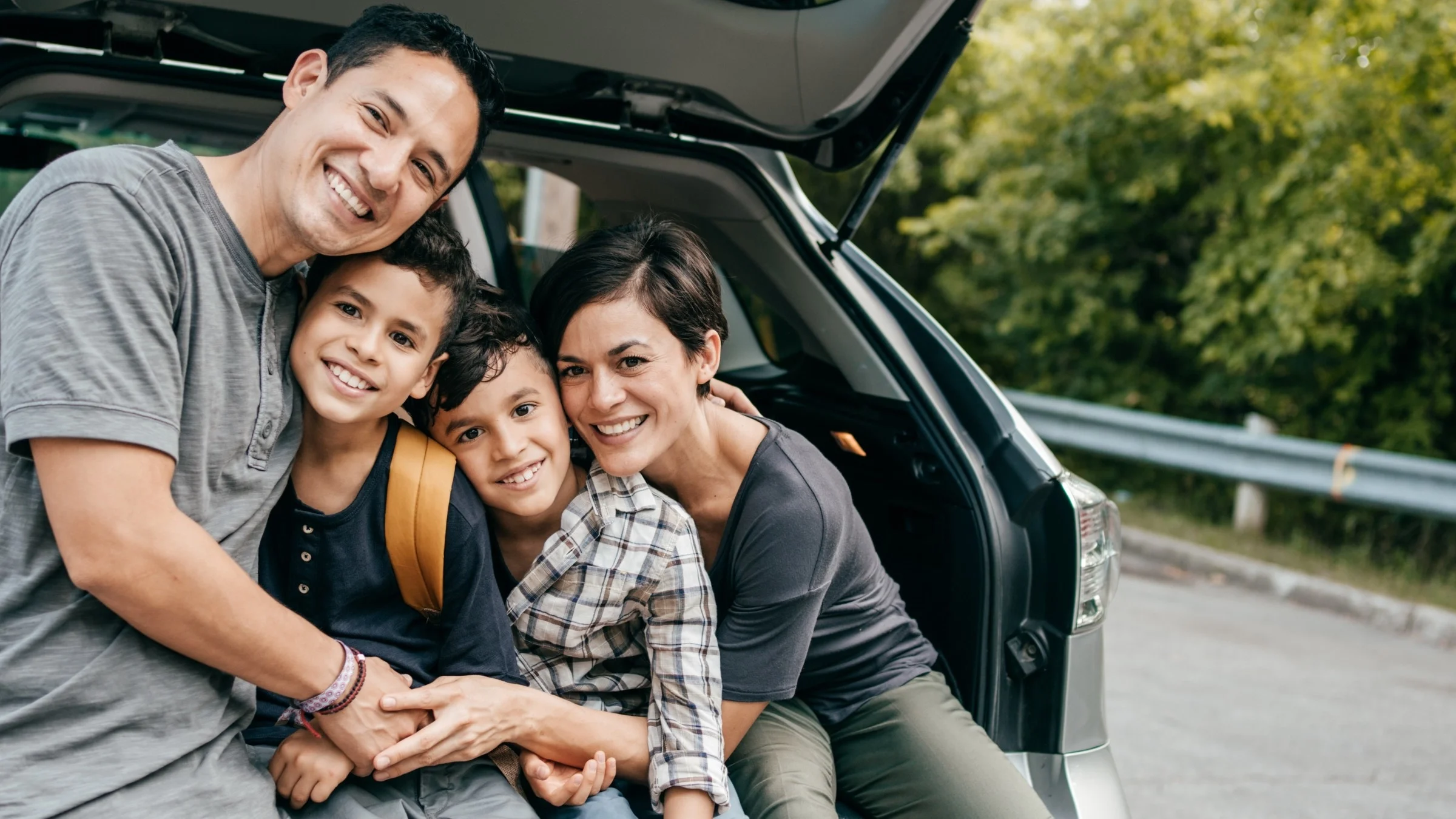 Portrait of a family with two kids sitting on the edge of the back trunk of a van.