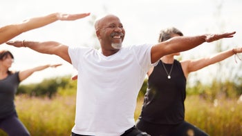 Health: Movement-exercise: older man doing yoga in field warrior pose 1184835694