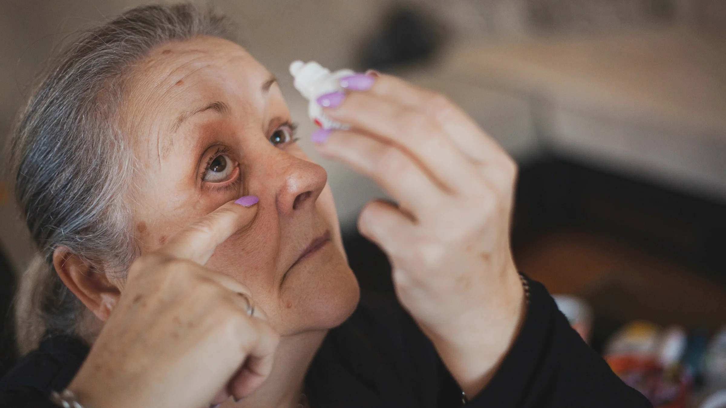 Senior woman putting in eye drops.
