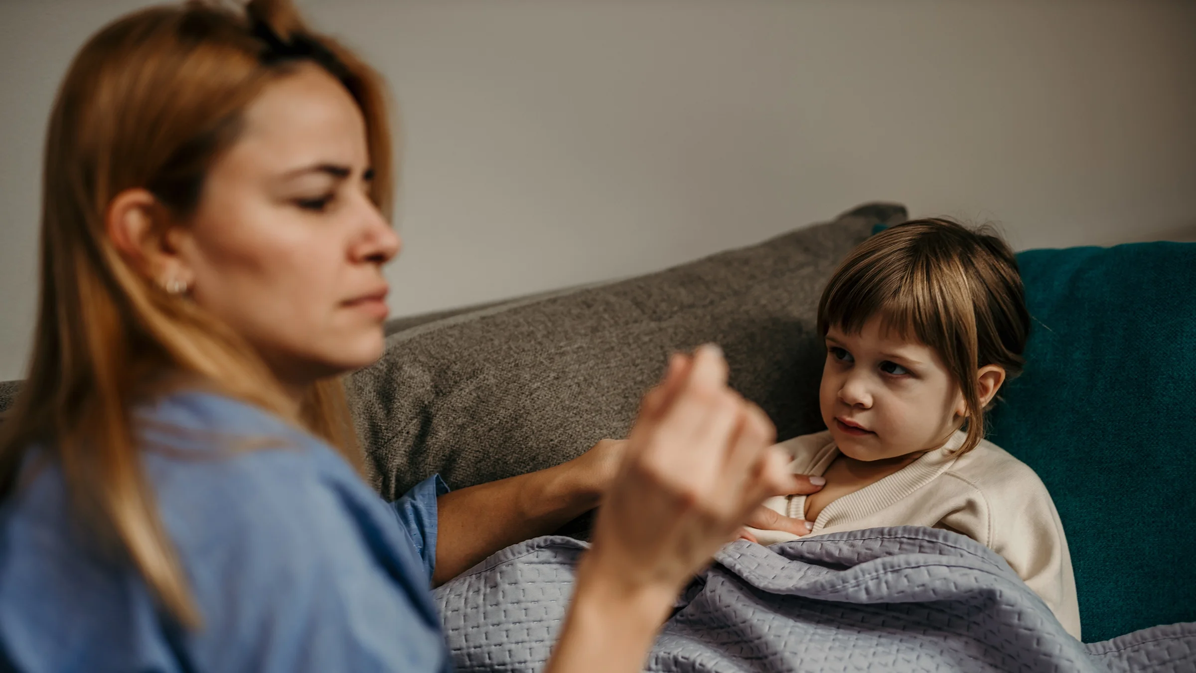 A woman looks at a thermometer while checking the temperature of her daughter. 