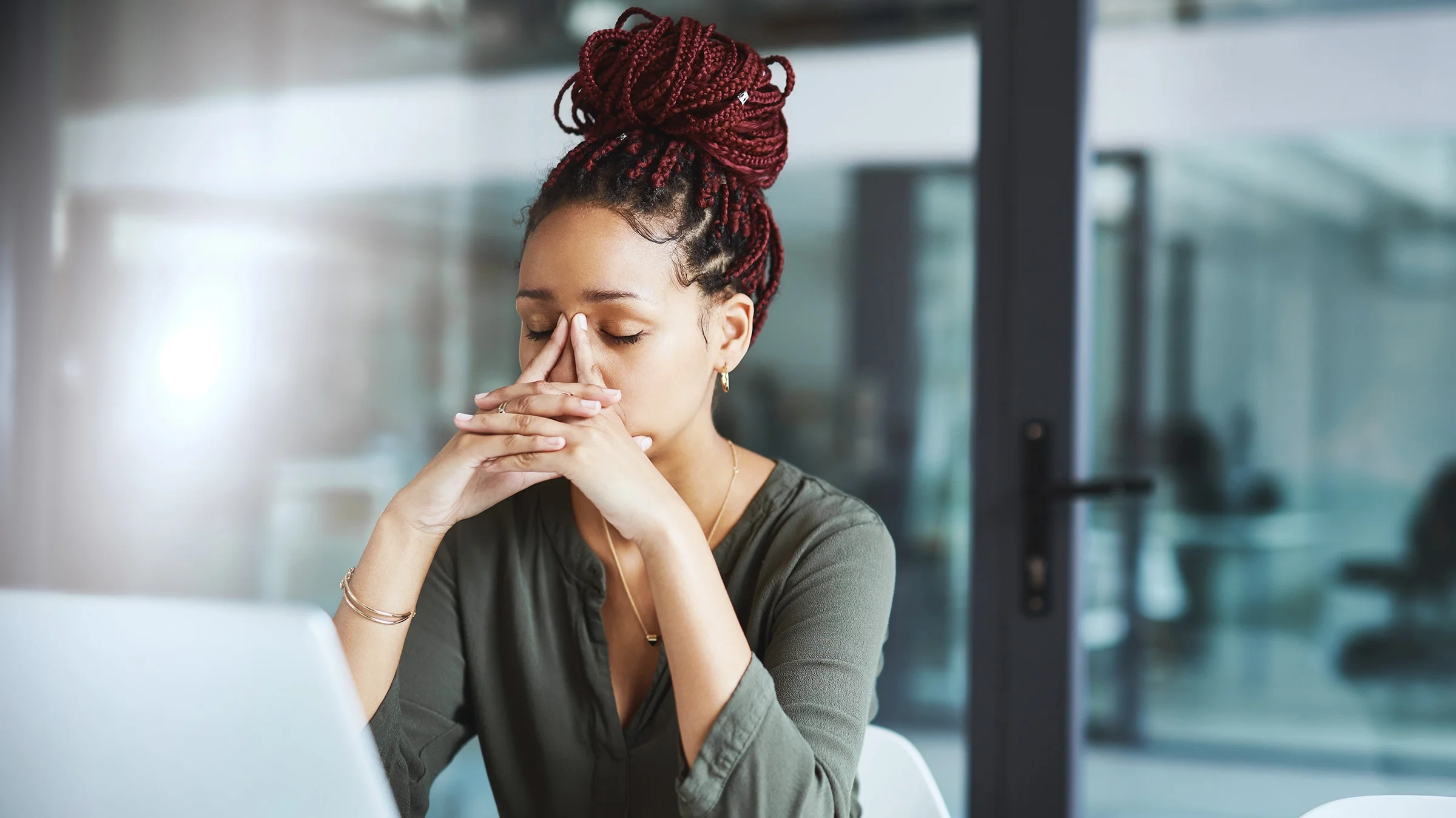 Young woman very stressed out at work. Her hands are on the bridge of her nose and forehead.