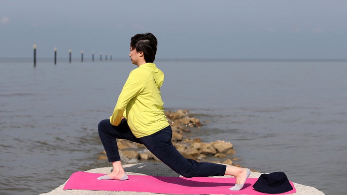 Woman doing lunge stretch outside near water.