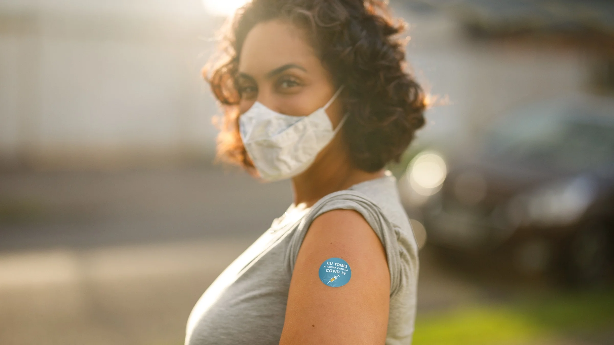 Portrait of young woman in face mask showing off her arm where she got the COVID-19 vaccine shot