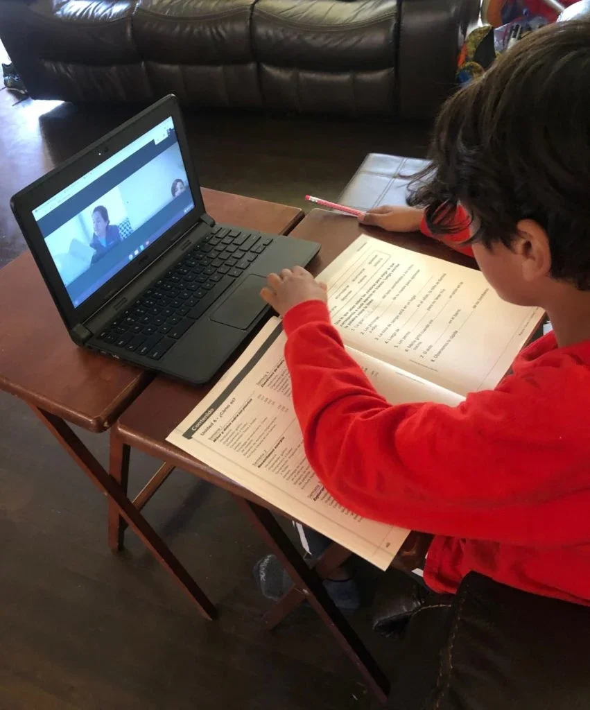 Kid sitting in front of laptop with textbook open