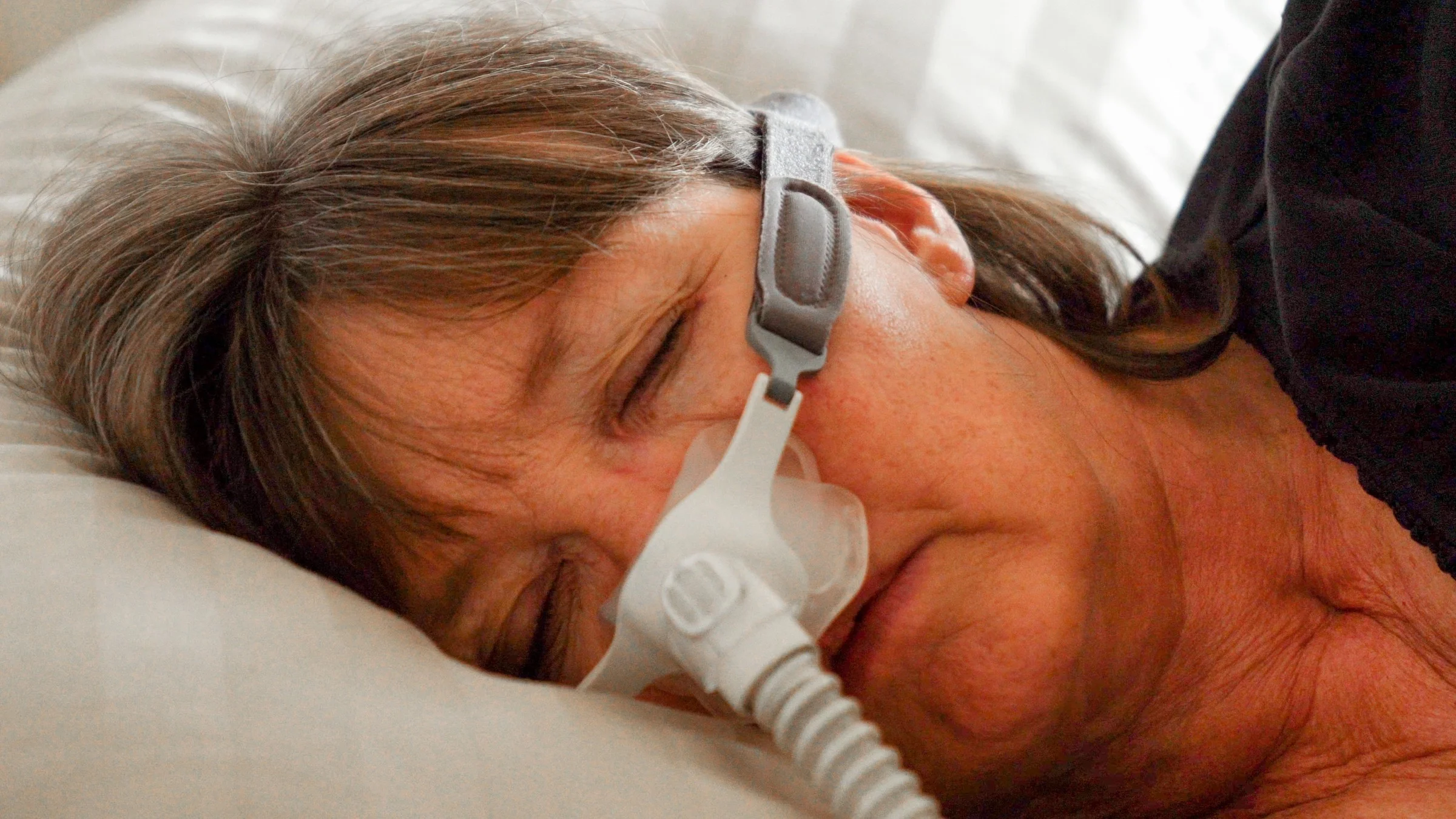 Close-up on a woman sleeping with a sleep apnea device on her nose and face.