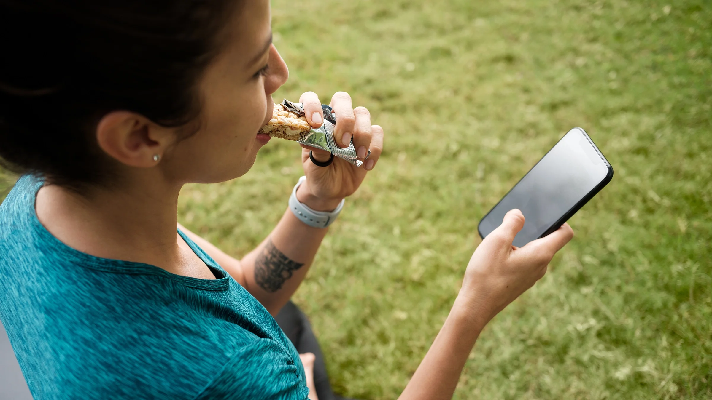 Woman eating protein bar and using a phone outdoors.