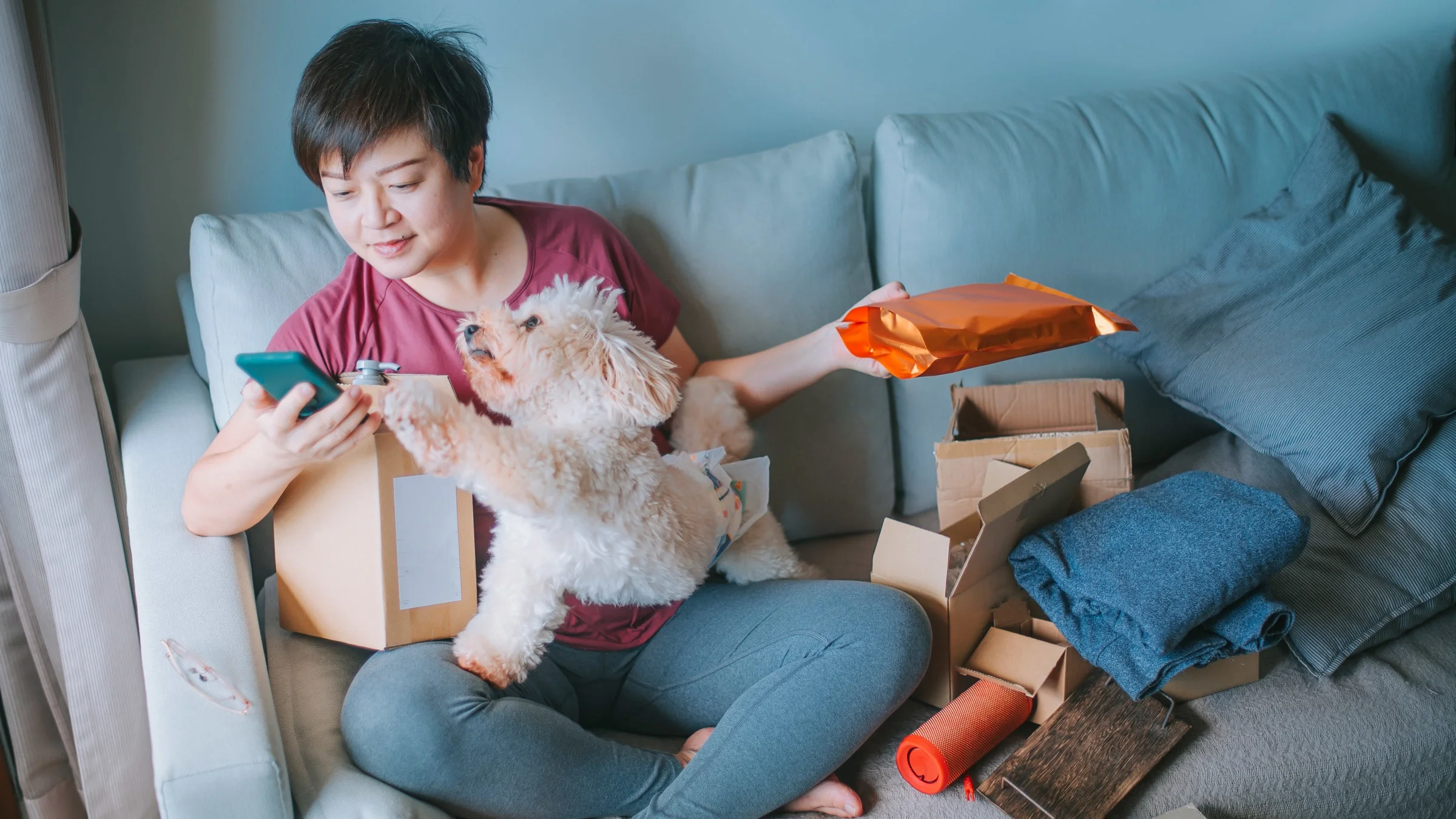 A person unpacking online purchases on their couch with their dog.