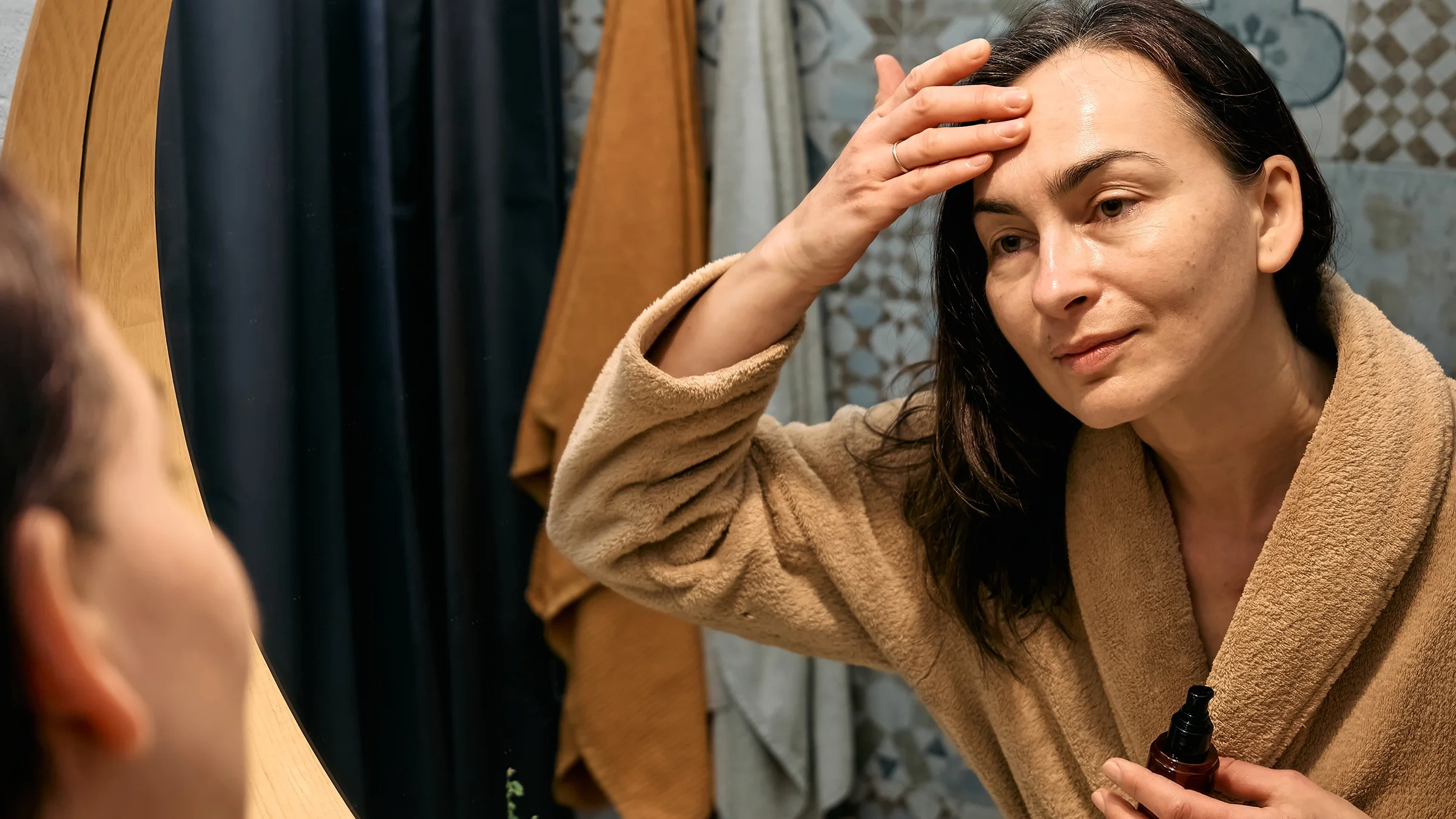 Woman in a bathrobe applies product to her forehead.