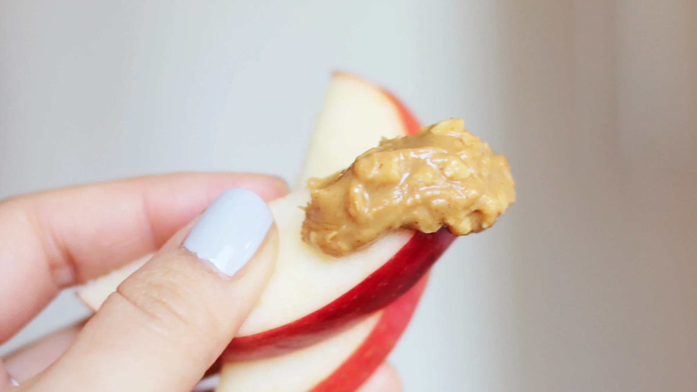 Hand holding sliced red apple with a dollop of crunchy peanut butter.