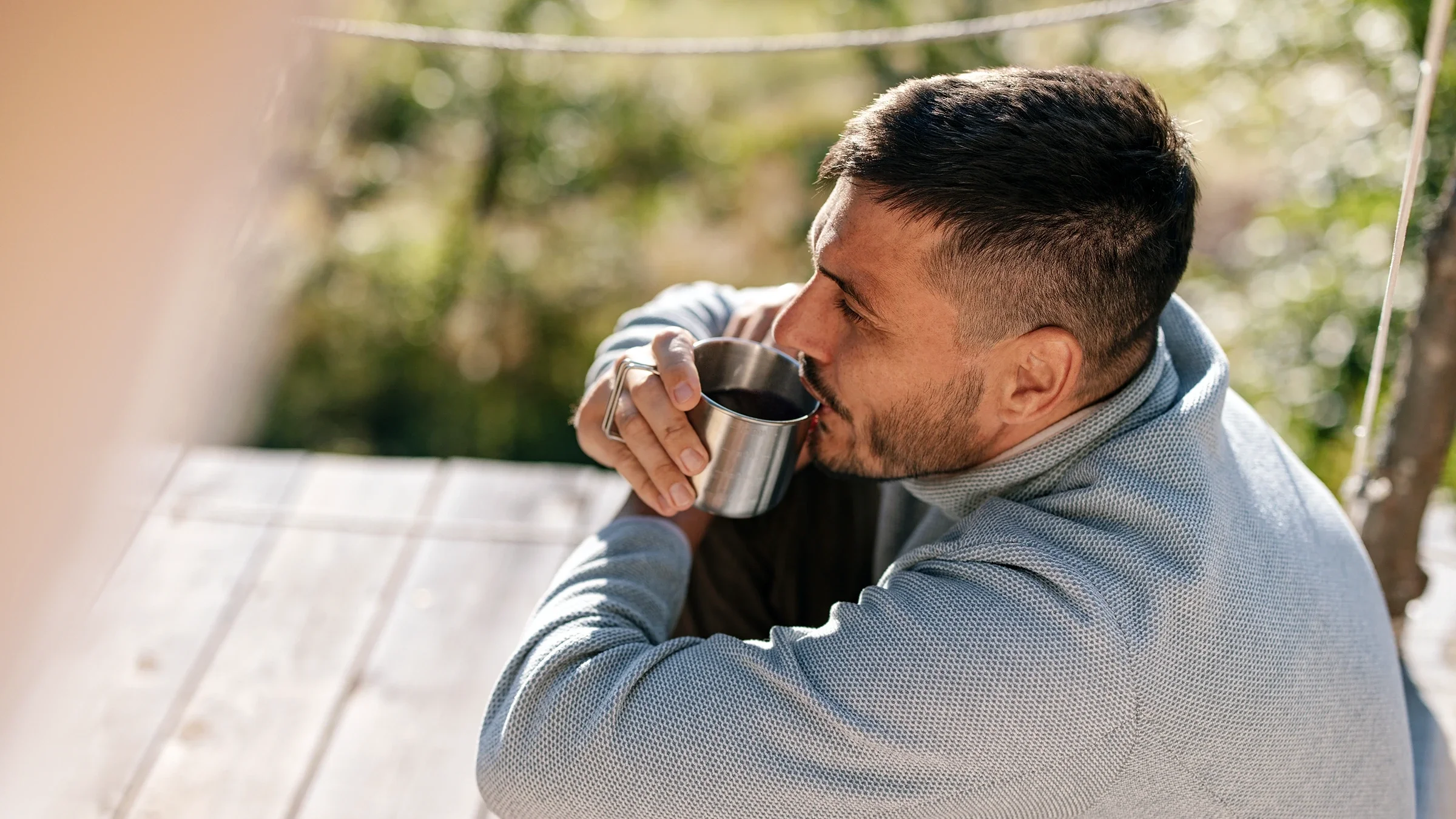 Man sits outdoors with a cup of coffee.