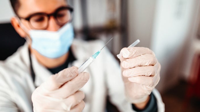 Close-up of a doctor preparing a syringe with a vaccine while wearing a blue medical face mask.