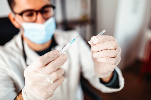 Close-up of a doctor preparing a syringe with a vaccine while wearing a blue medical face mask.