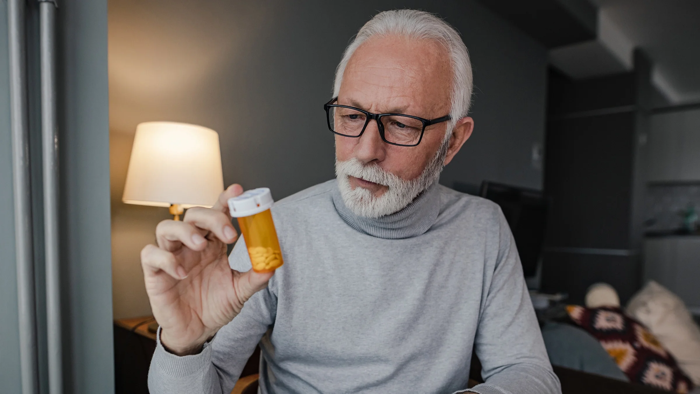 Senior man with white hair and beard reviewing his prescription bottle.