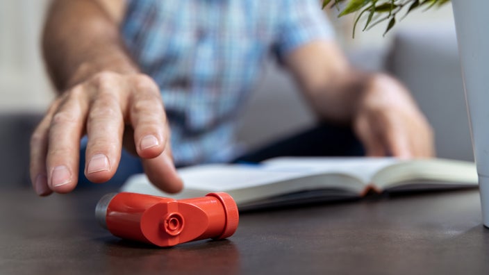 Close-up of a man's hand reaching for an inhaler on the table.