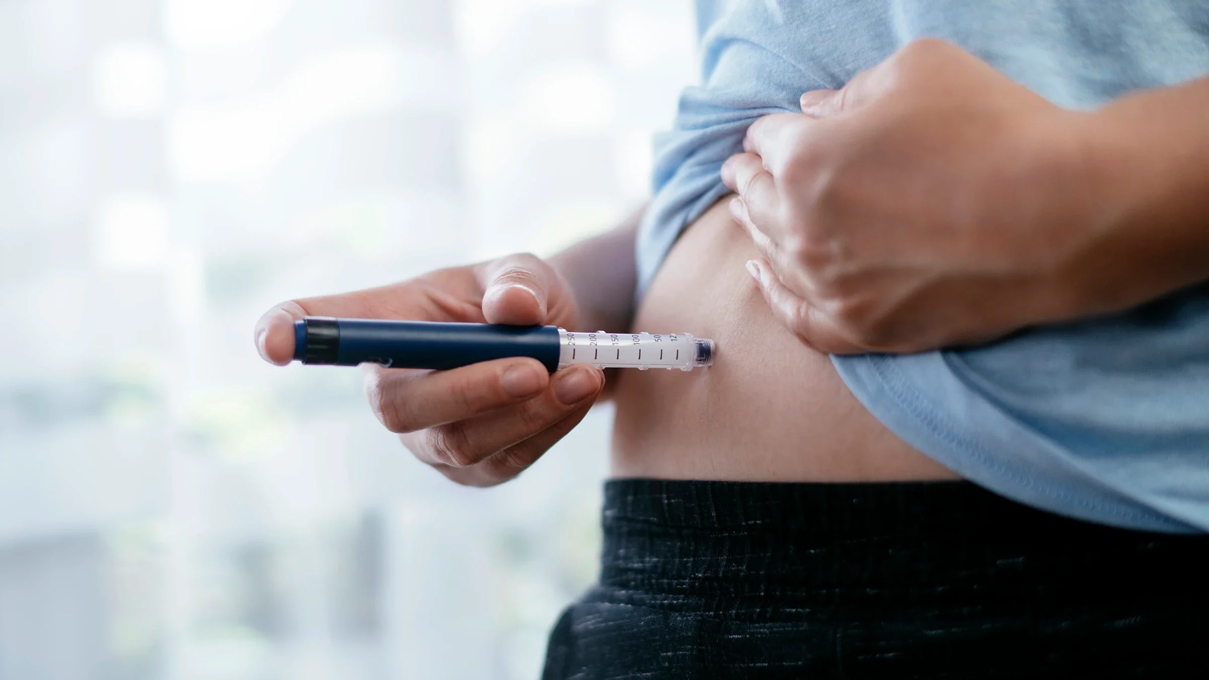 Close-up on a person using an injection pen on their abdomen.
