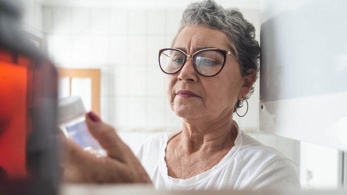 Close-up of an elderly woman looking at a bottle of supplements in her medicine cabinet.