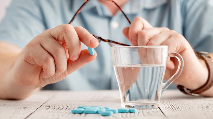 Man holding blue pill with glass of water