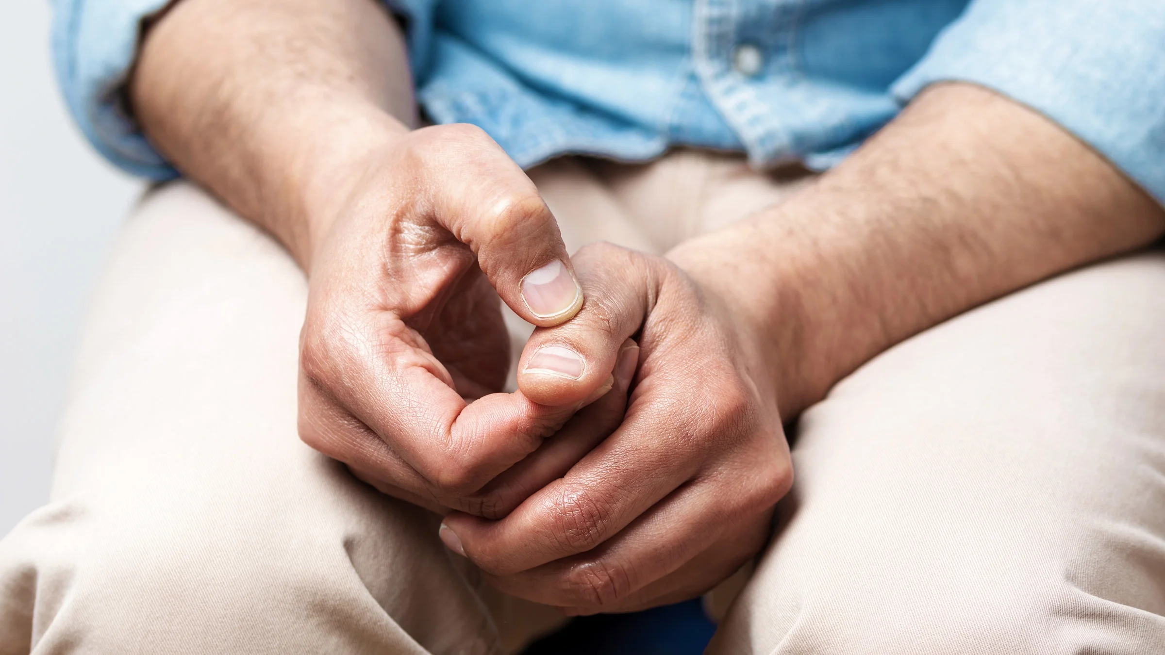 Cropped photo of an anxious person sitting on a couch, zoomed in on their thumbs twiddling.