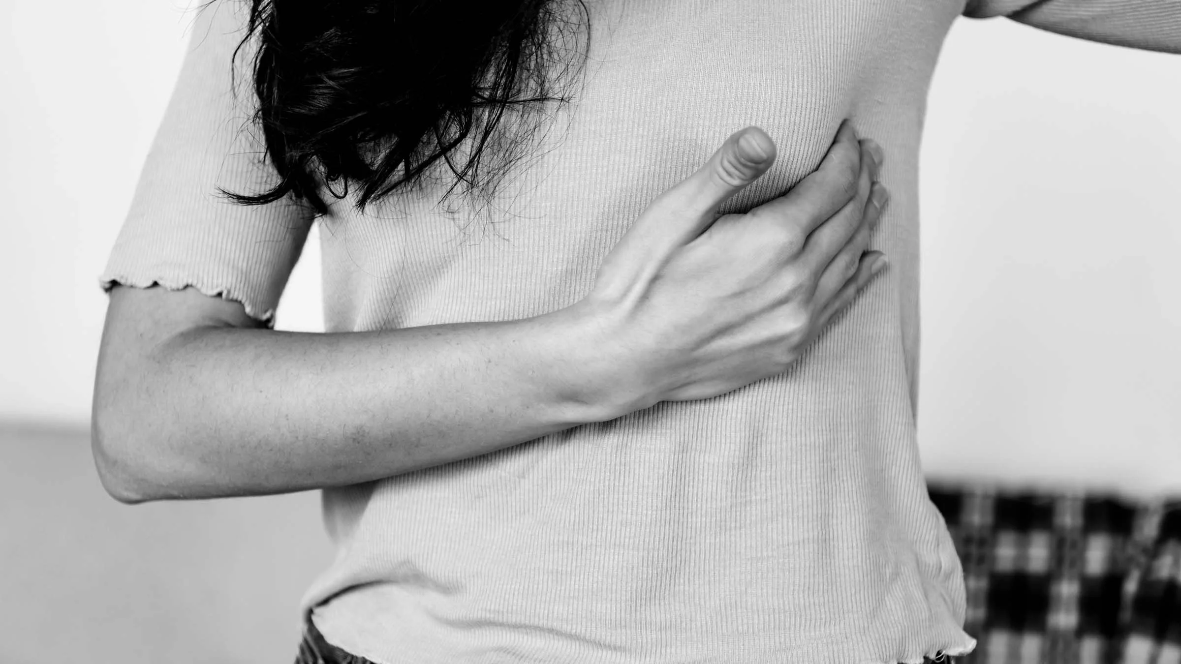 Black and white cropped close-up of a woman rubbing the side of her breast.