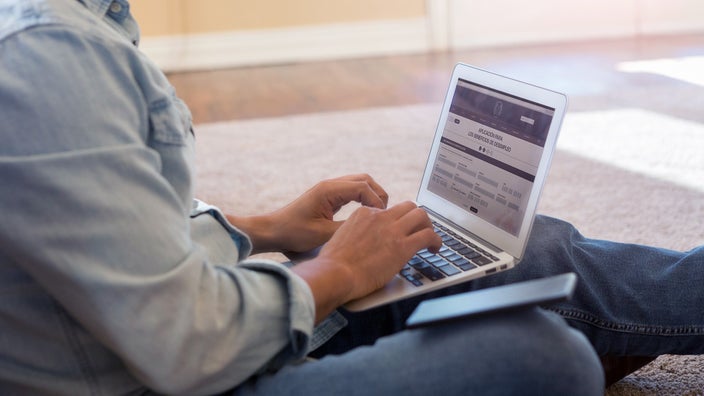 Cropped image of a man sitting on the floor with his laptop filling out medical paperwork online.