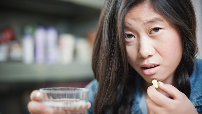 An anxious/tired-looking person holding a pill and a glass of water.