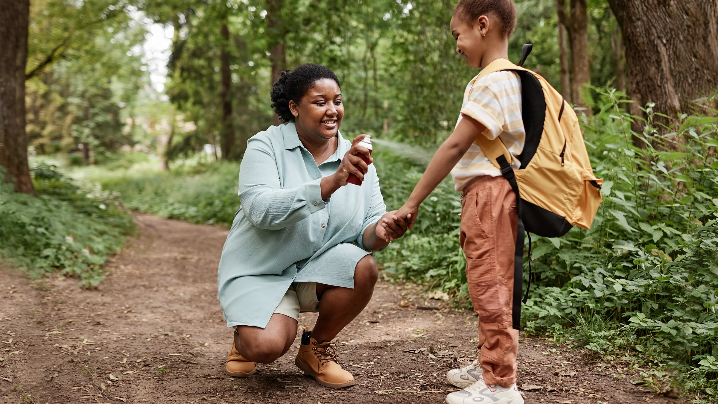 Woman spraying bug spray on child while hiking outdoors.