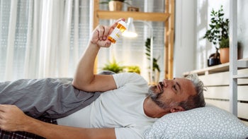 Sleep: man reading Rx bottle in bed 1782385780
