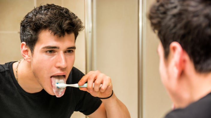 A mirror reflection of someone brushing their tongue.