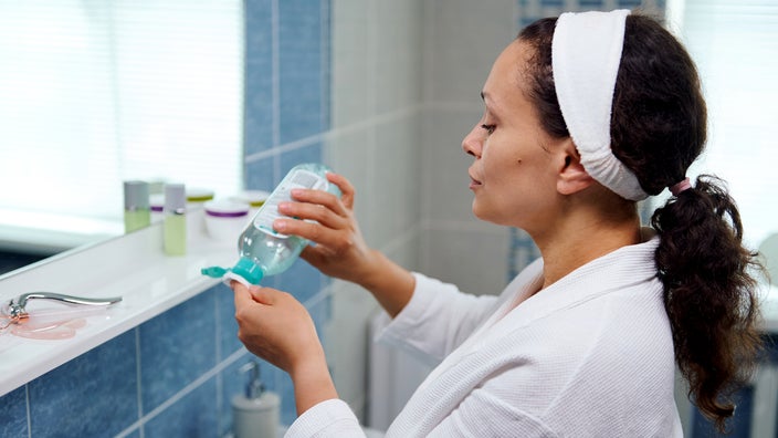 A woman pours cleanser on a cotton pad. 