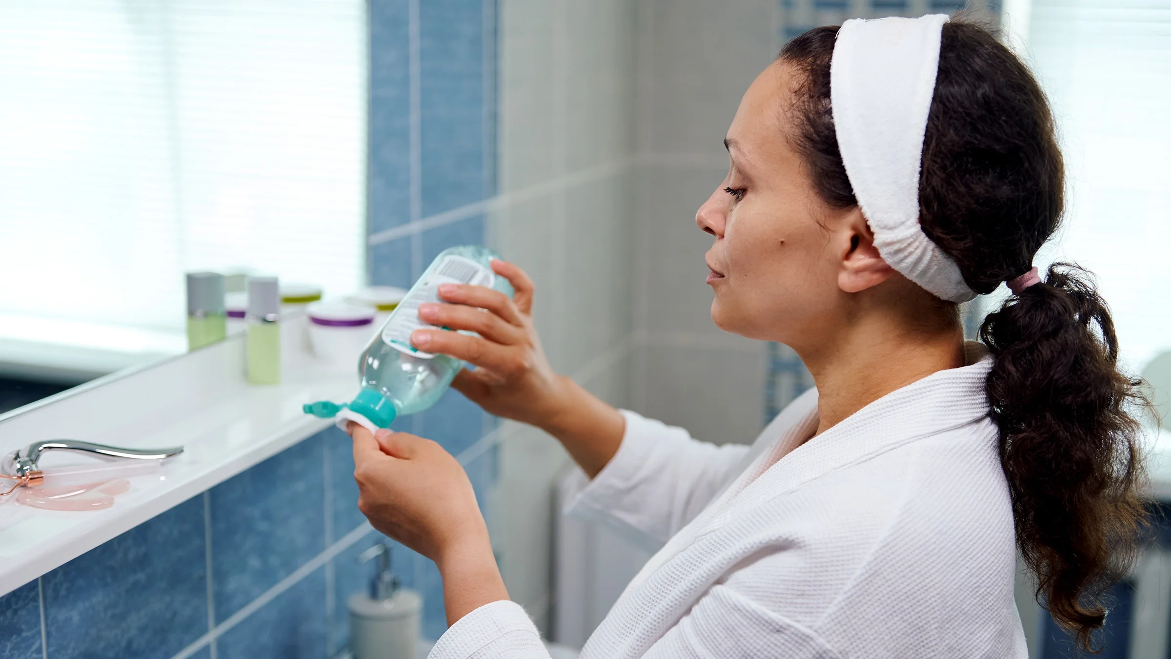 A woman pours cleanser on a cotton pad.