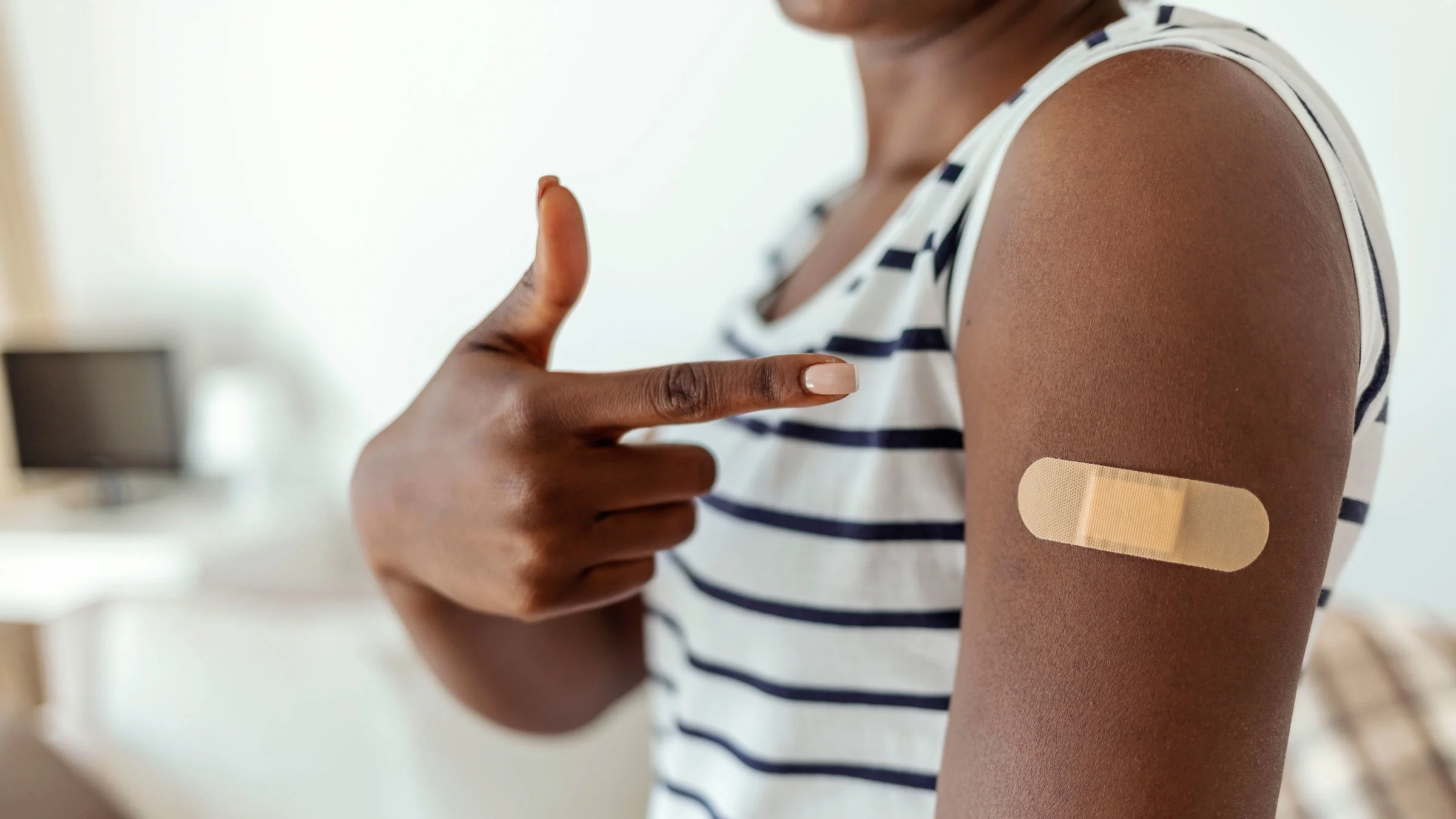 A person points their finger to the band-aid on their upper arm after a vaccine shot.